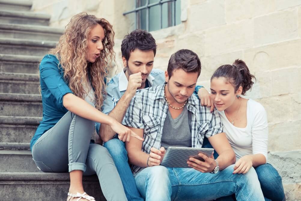 Grupo de persones están sentadas en escaleras haciendo jugadas en una tablet