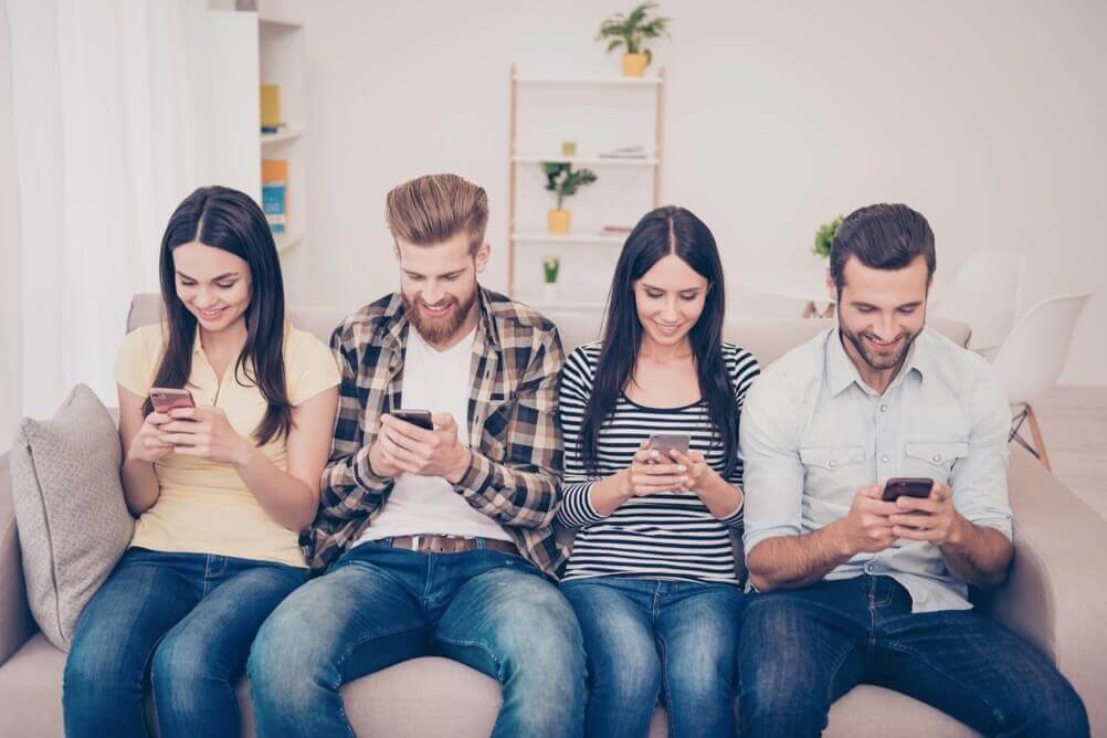 Grupo de personas están sentadas en un sofa jugando la lotería con sus celulares