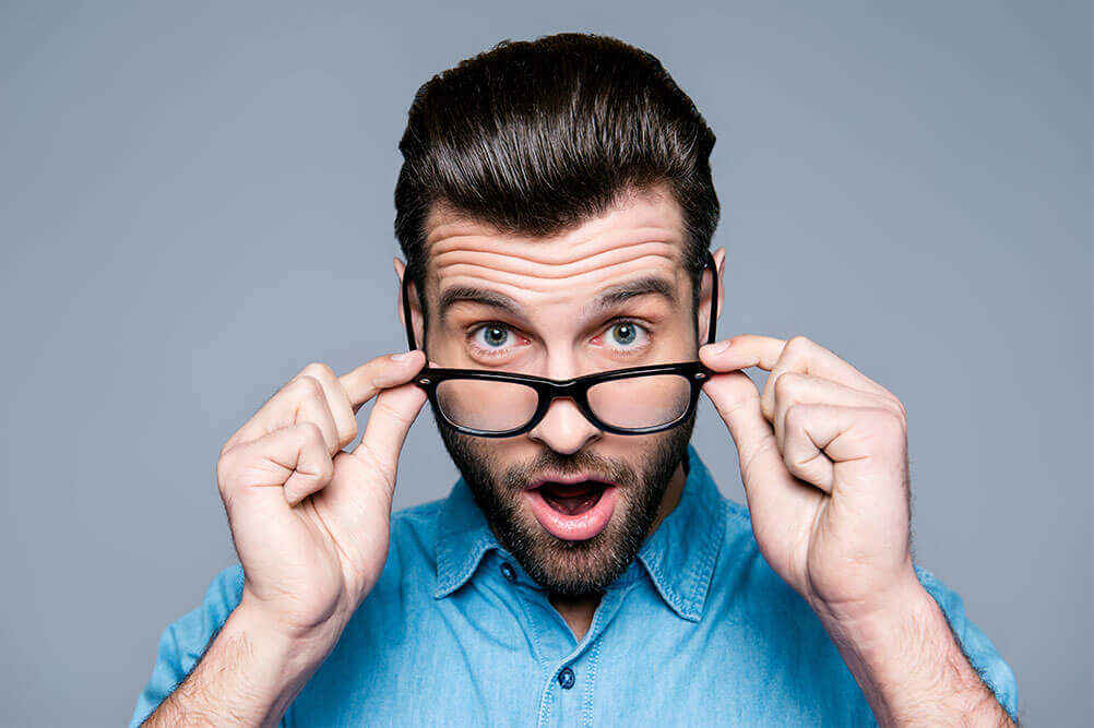 Hombre con camisa azul se quita sus gafas sorprendido