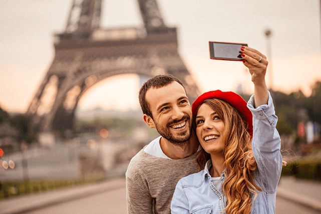 Una pareja feliz tomándose un selfie frente a la Torre Eiffel