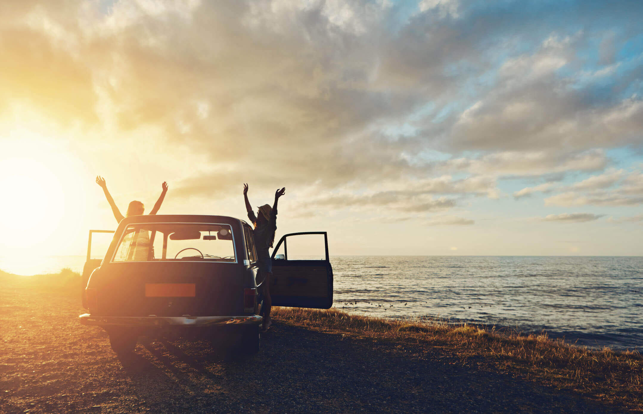 Dos chicas levantan las manos fuera de un coche en la playa