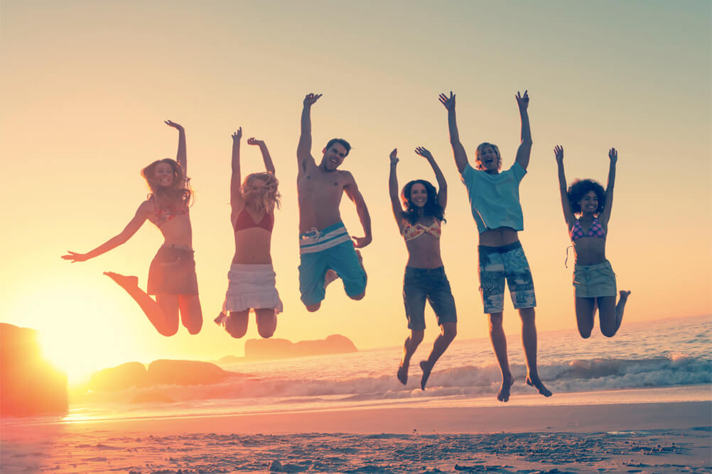 Grupo de  personas saltan alegres  en la playa con el atardecer de fondo