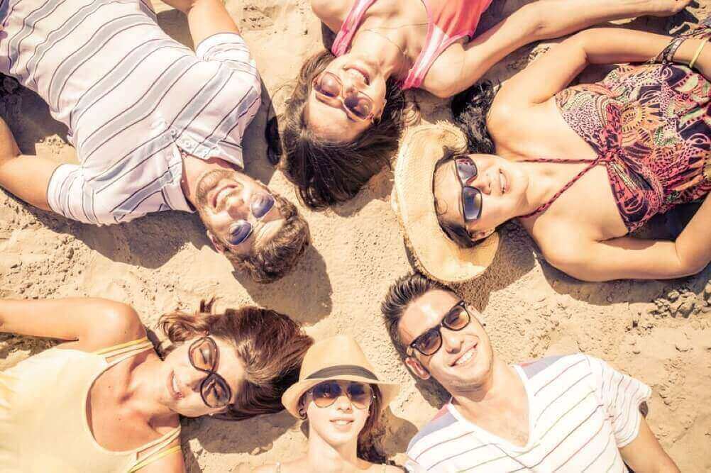 grupo de personas están acostados en círculo  sobre la arena y están sonriendo